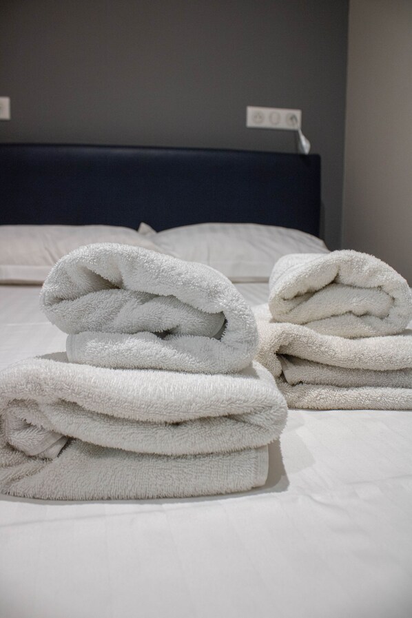 A neatly made bed with white linens and a folded white towel on top.