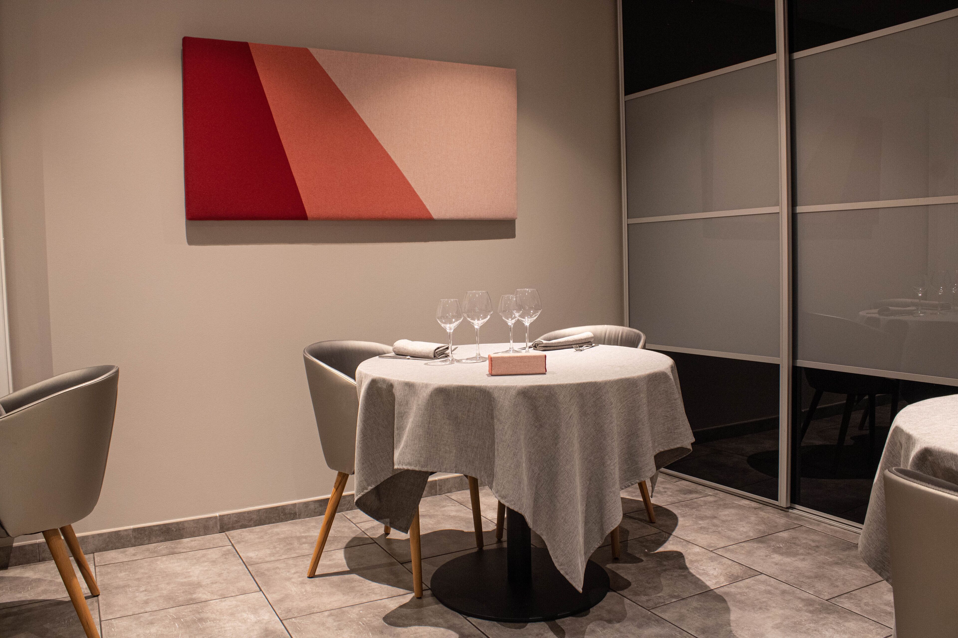 A dining area with a round table, chairs, and a red and beige abstract painting on the wall.