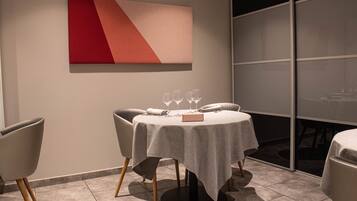 A dining area with a round table, chairs, and a red and beige abstract painting on the wall.