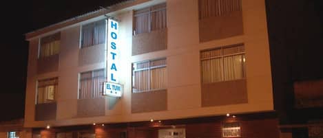 Un edificio de dos pisos con un letrero que dice "HOSTAL EL TUMI" en la entrada.