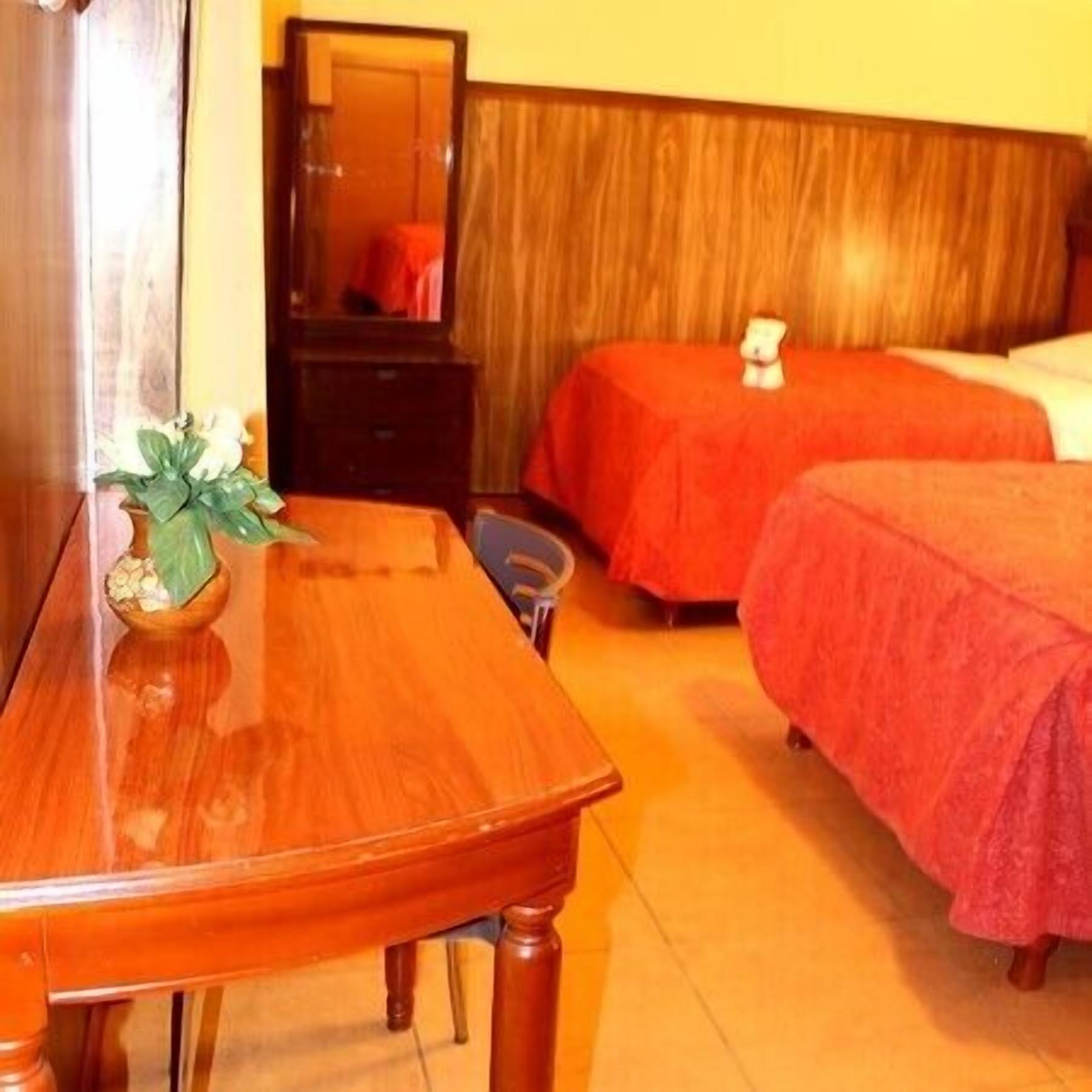 Habitación de hotel con una cama de madera, un aparador de madera y una pequeña mesa con una planta.