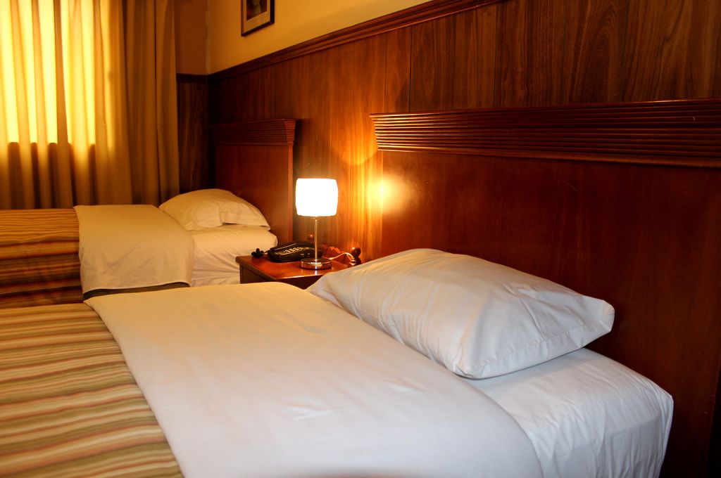 A hotel room with two beds, a nightstand with a lamp, and wooden paneling on the walls.