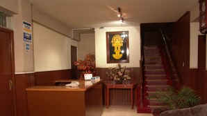 A reception area with a wooden desk, a telephone, a vase with flowers, a framed picture on the wall, and a staircase. - Hotel El Tumi 2 (Huaraz)