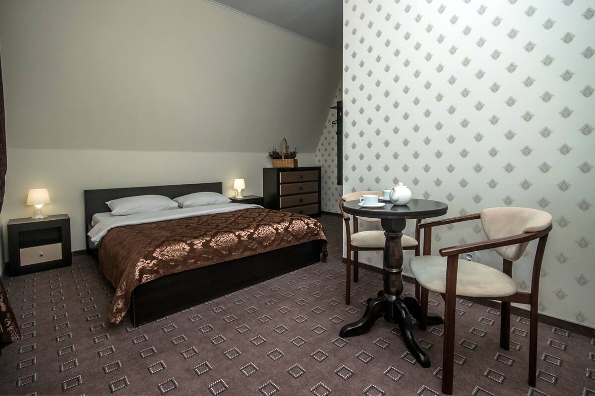 A hotel room with a bed, bedside tables, a small table with chairs, and a patterned wall.
