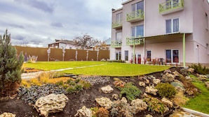 A multi-story building with balconies, a well-maintained garden with various plants and rocks, and a cloudy sky. - Ryleev Hotel (Kharkiv)
