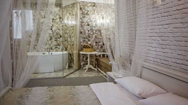 A bedroom with a bed, a nightstand, a bedside table with a lamp, and a bathroom with a bathtub and shower. - Ryleev Hotel (Kharkiv)