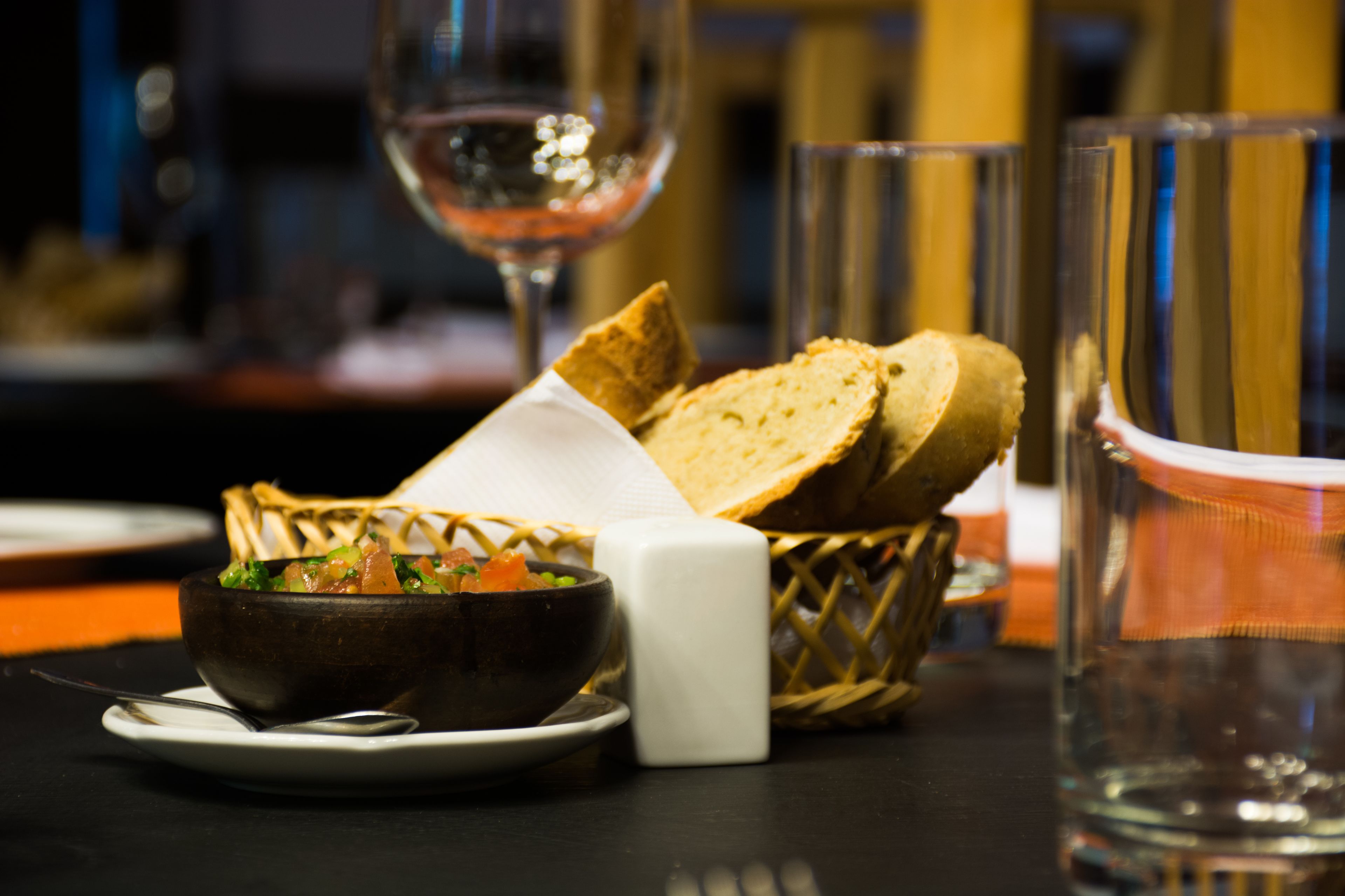 A dining table with a bowl of soup, slices of bread, a salt shaker, and a glass of water.
