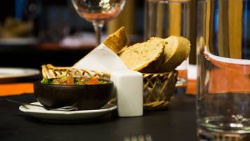 A dining table with a bowl of soup, slices of bread, a salt shaker, and a glass of water.