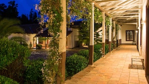 Un espacio exterior cubierto con un sendero de ladrillo, columnas de madera y vegetación.