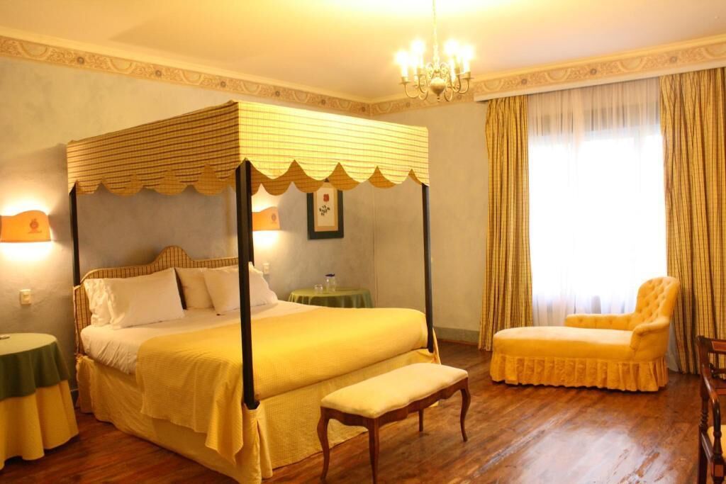 A four-poster bed with a canopy, a bench, a chair, and a small table with a lamp.
