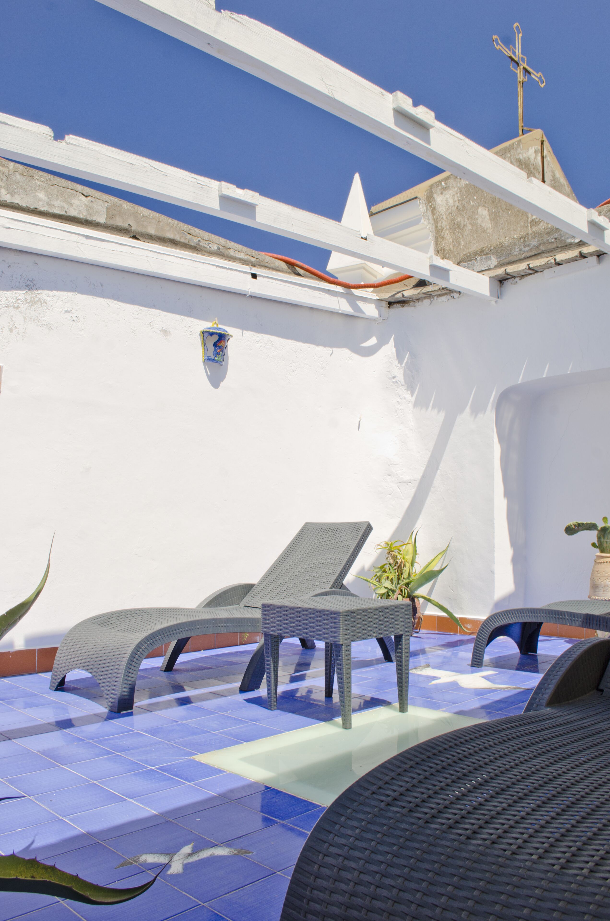 Una terraza en la azotea con dos sillones, una planta en maceta y un suelo de baldosas azules.