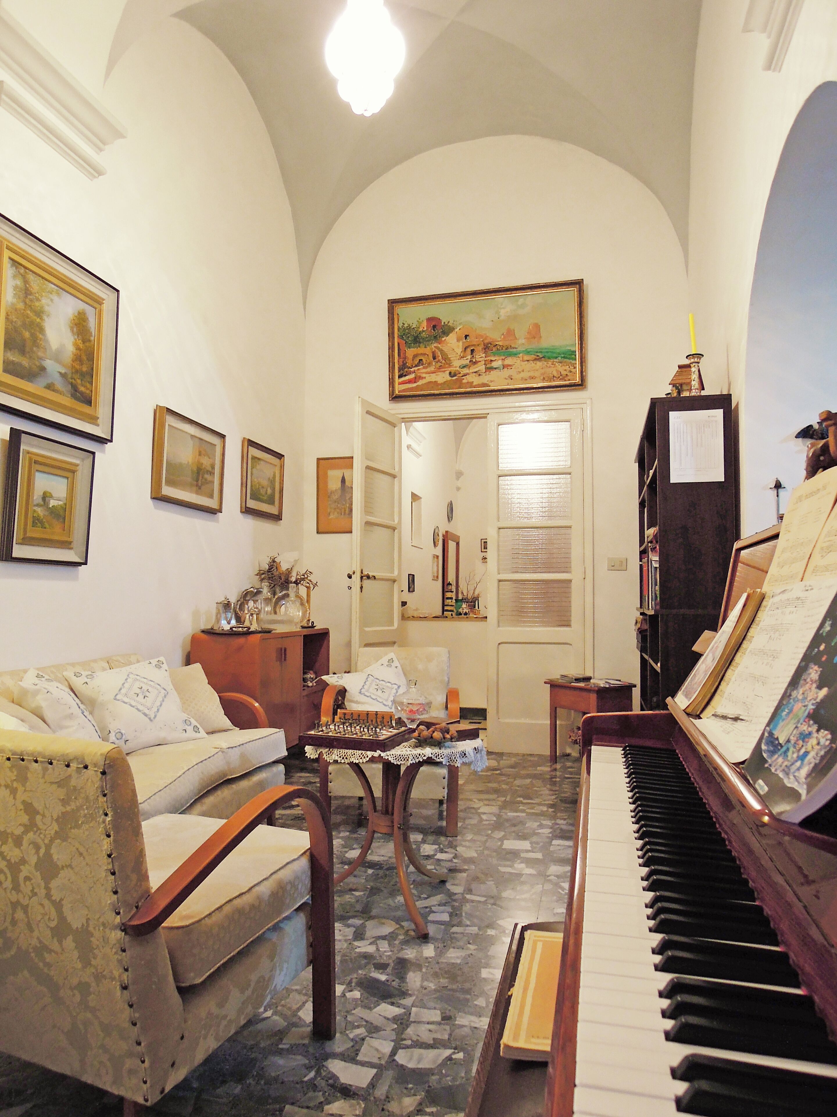 A cozy living room with a piano, a sofa, a chess table, and framed pictures on the walls.