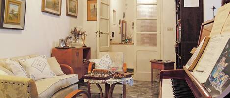 A cozy living room with a piano, a sofa, a chess table, and framed pictures on the walls.