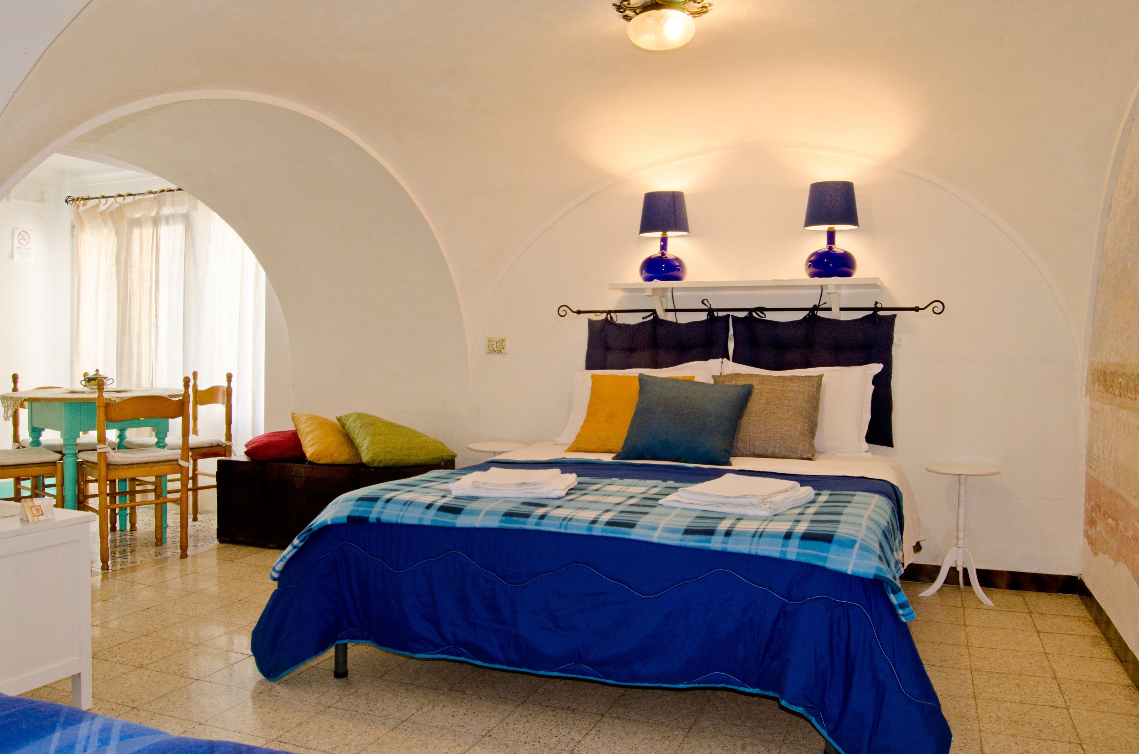 A bedroom with a bed, two bedside lamps, a small table, and a chair.
