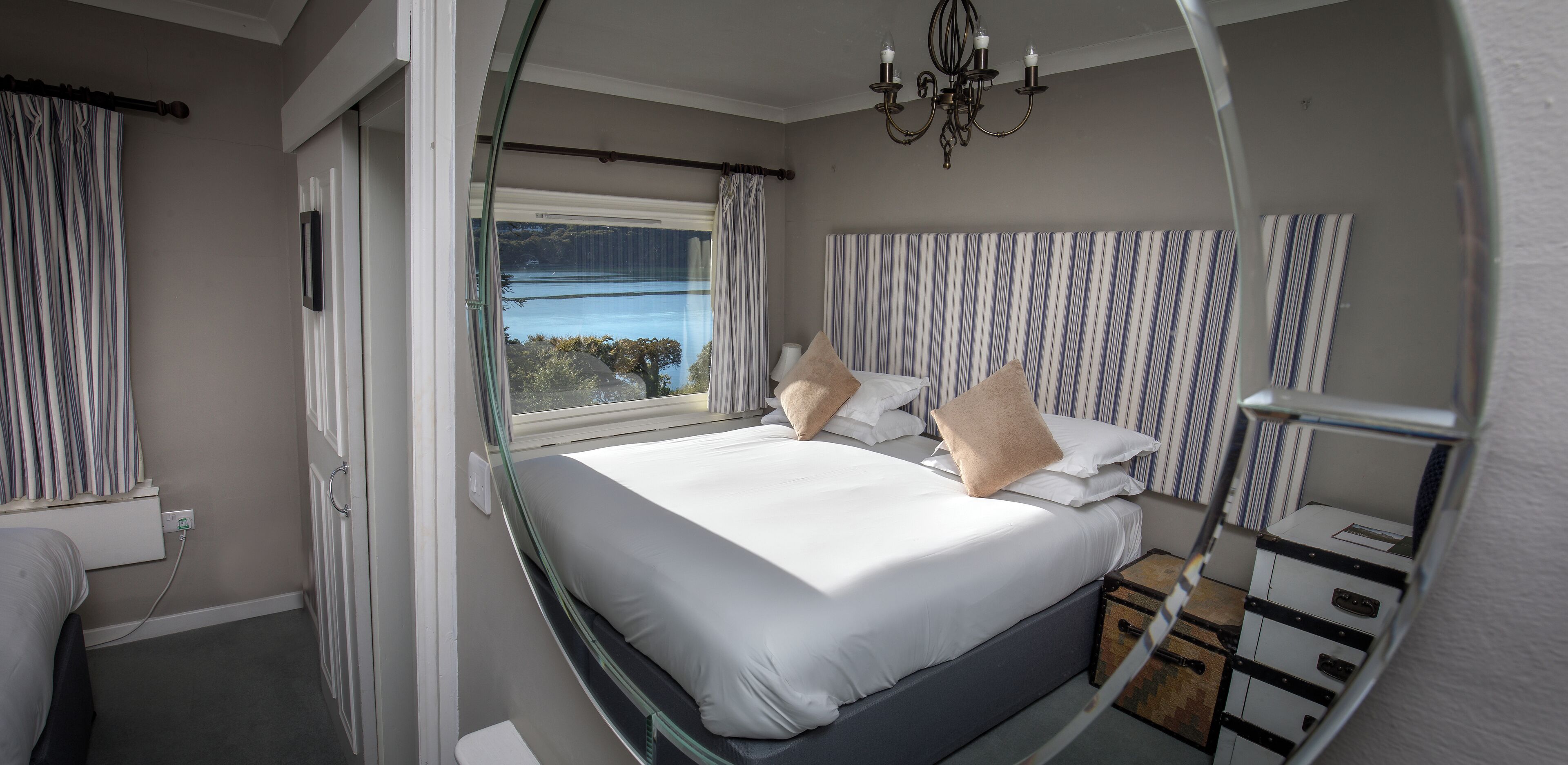 Ein Schlafzimmer mit Bett, einem Vorhangfenster, einer Chandelüster und Blick ins Freie.