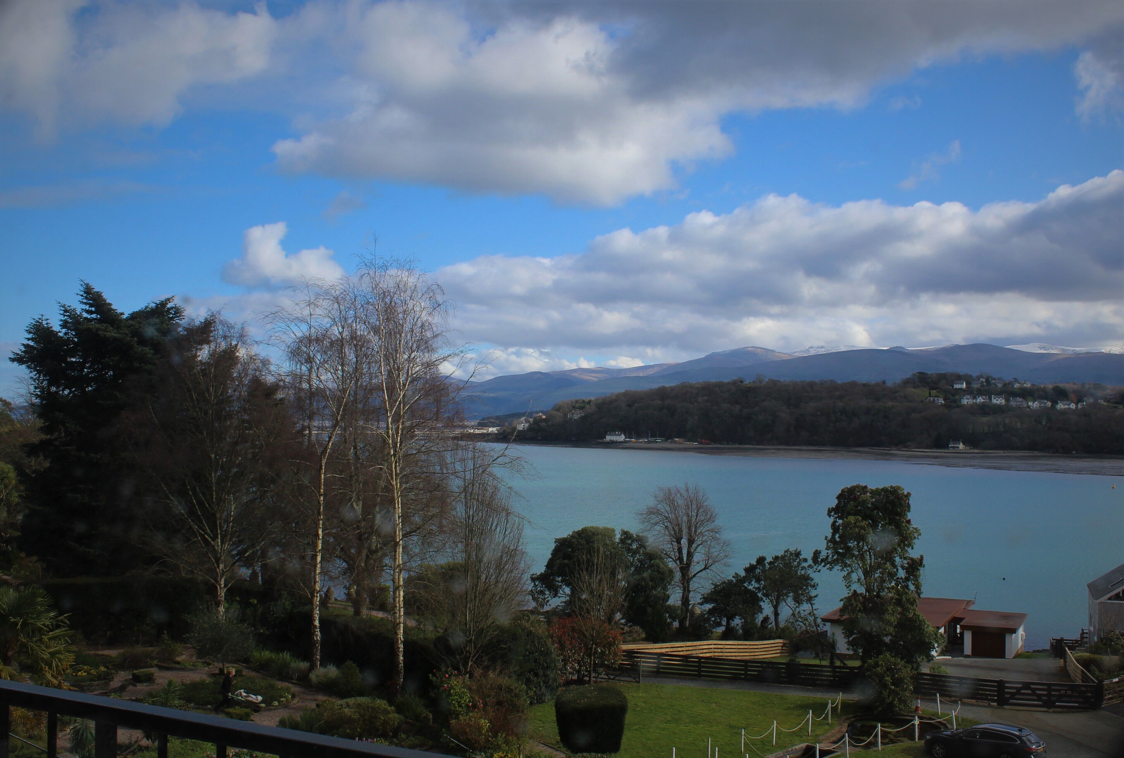 A lakeside view with mountains in the background, a wooden fence, and a building with a red roof.