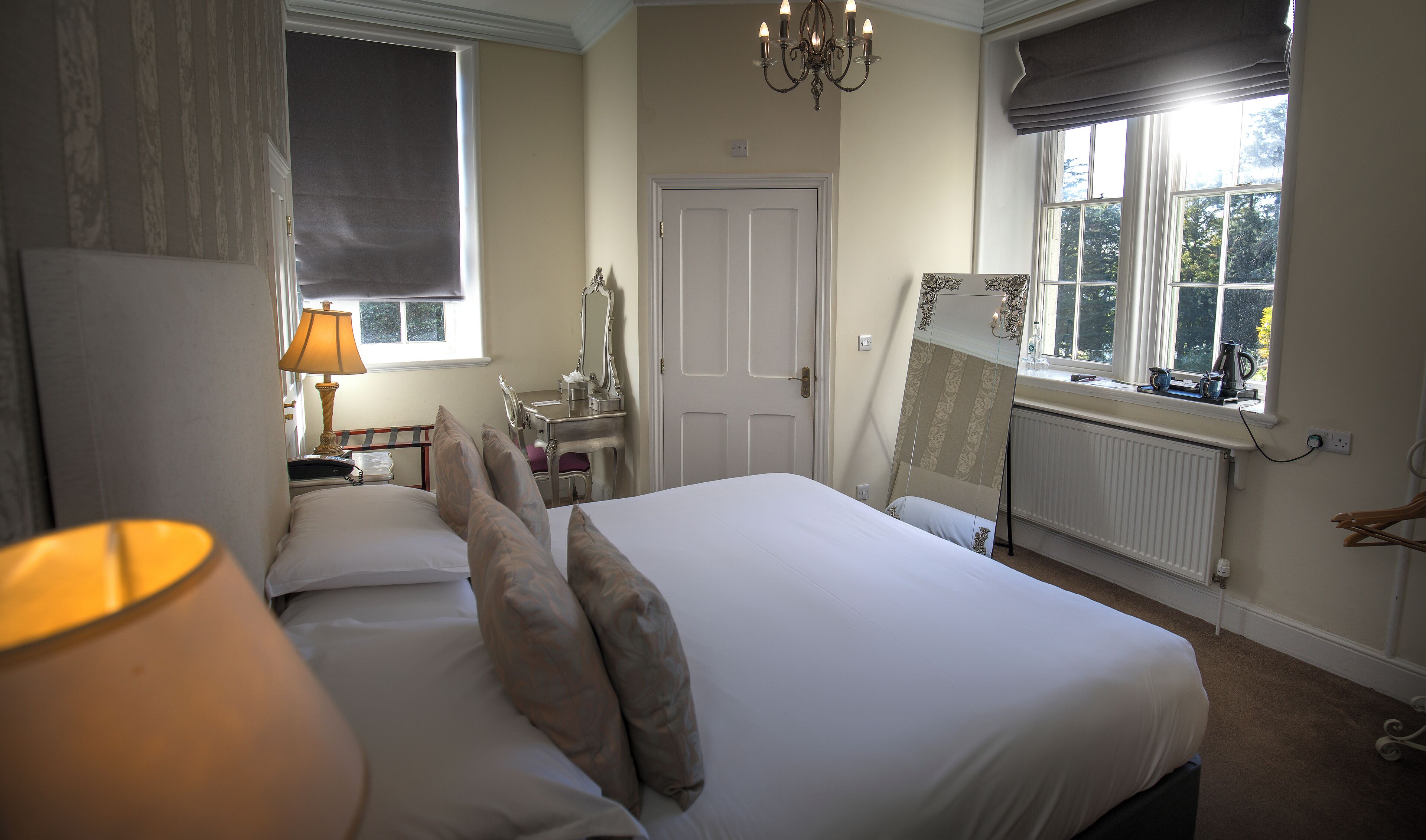 Une chambre d’hôtel comprenant un lit, une lampe de chevet, une commode, un miroir, une fenêtre et un radiateur.