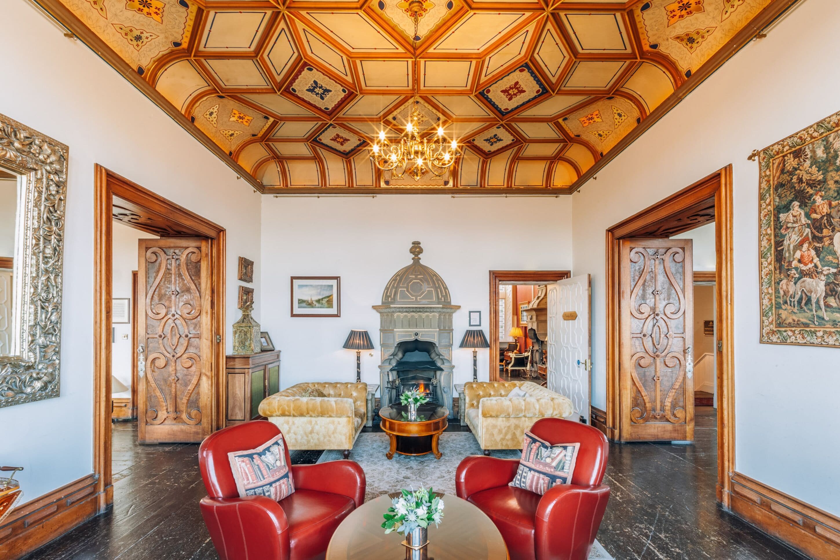A grand room with a high ceiling, ornate woodwork, a fireplace, and red leather chairs.