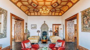 A grand room with a high ceiling, ornate woodwork, a fireplace, and red leather chairs.