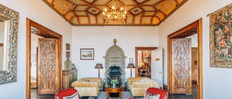 A grand room with a high ceiling, ornate woodwork, a fireplace, and red leather chairs.