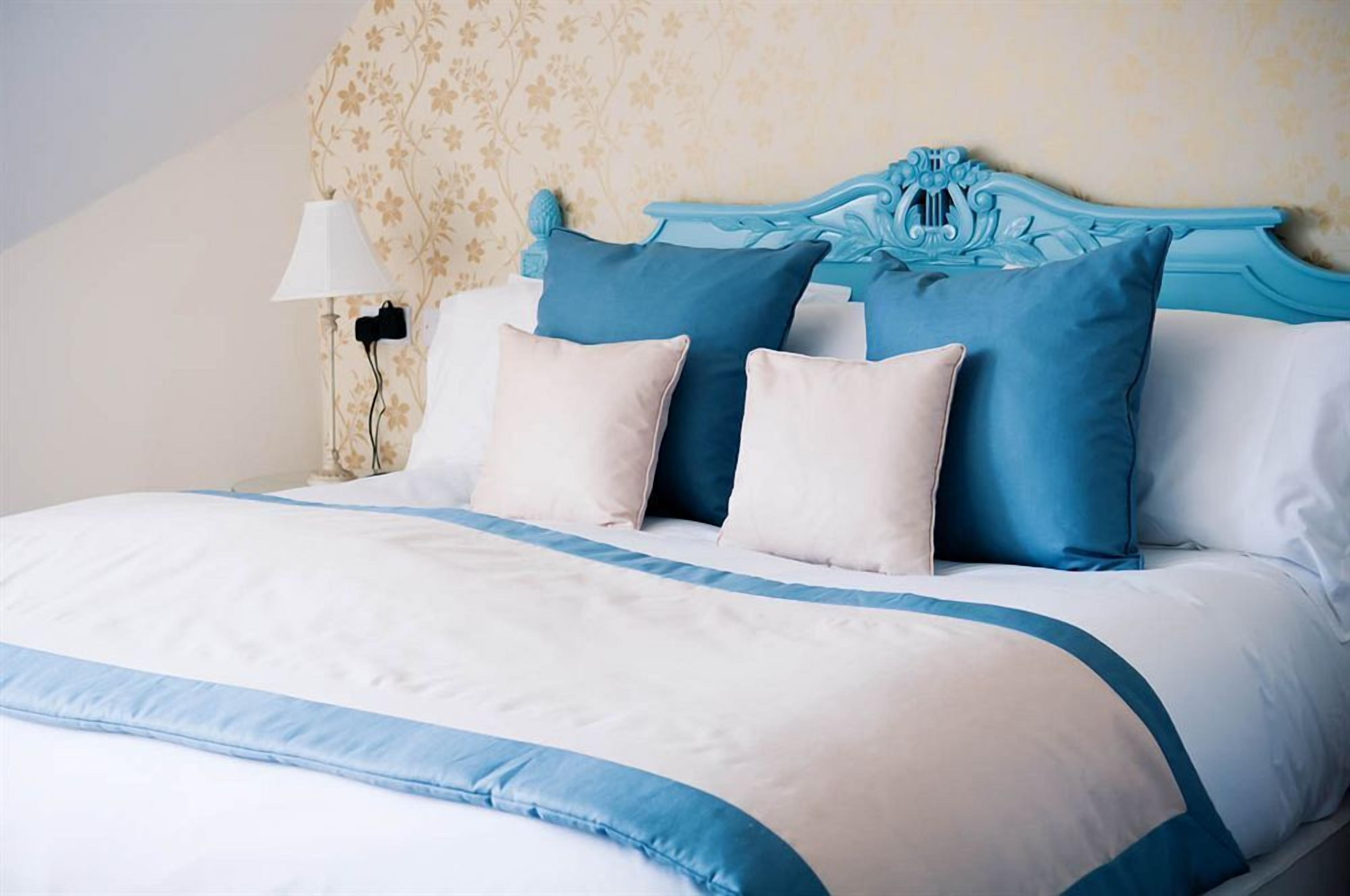 A bed with a blue and white bedspread, a decorative headboard, and a bedside lamp.