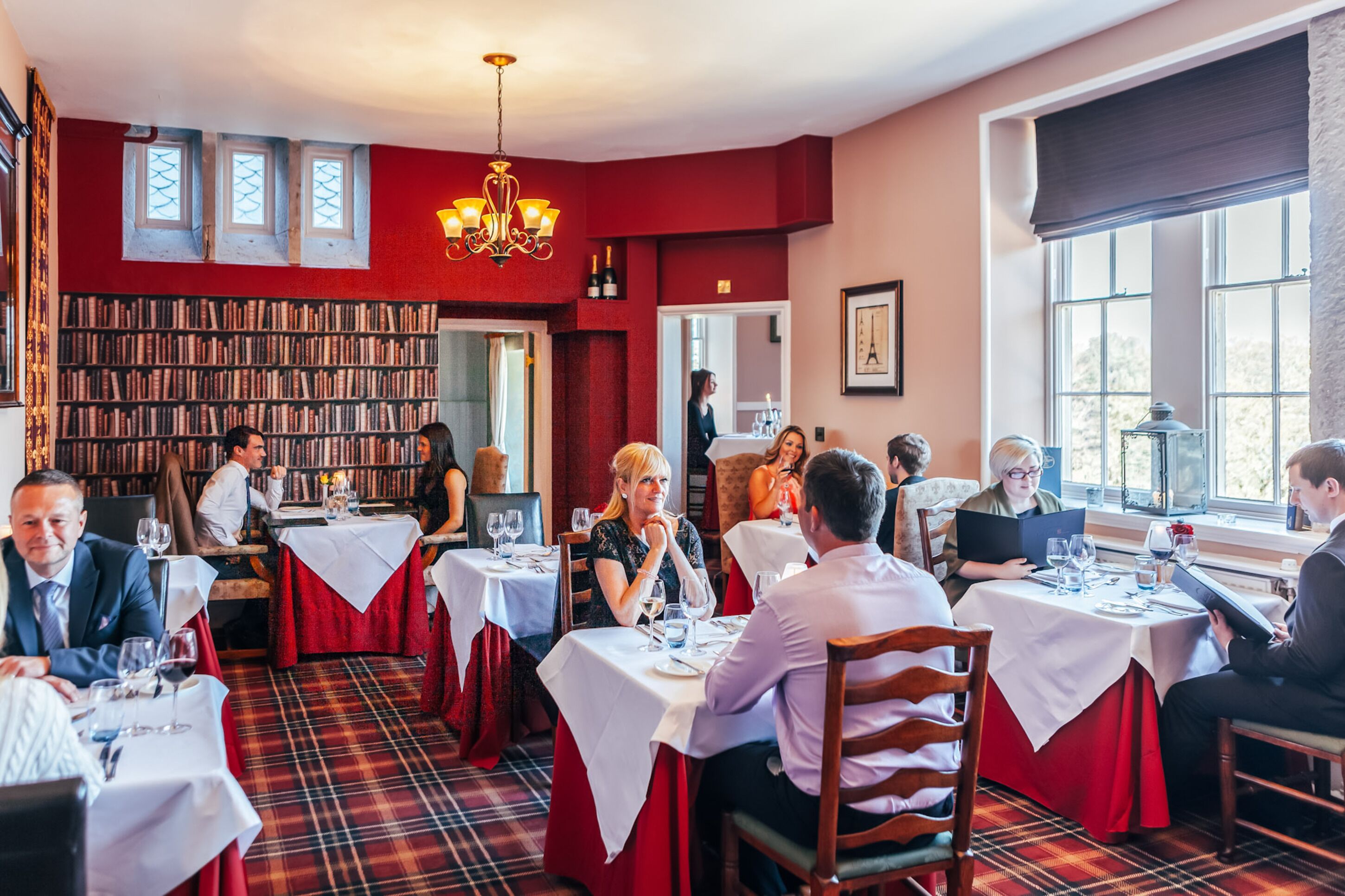 Un restaurante con paredes rojas, una amplia estantería y comensales cenando en mesas.