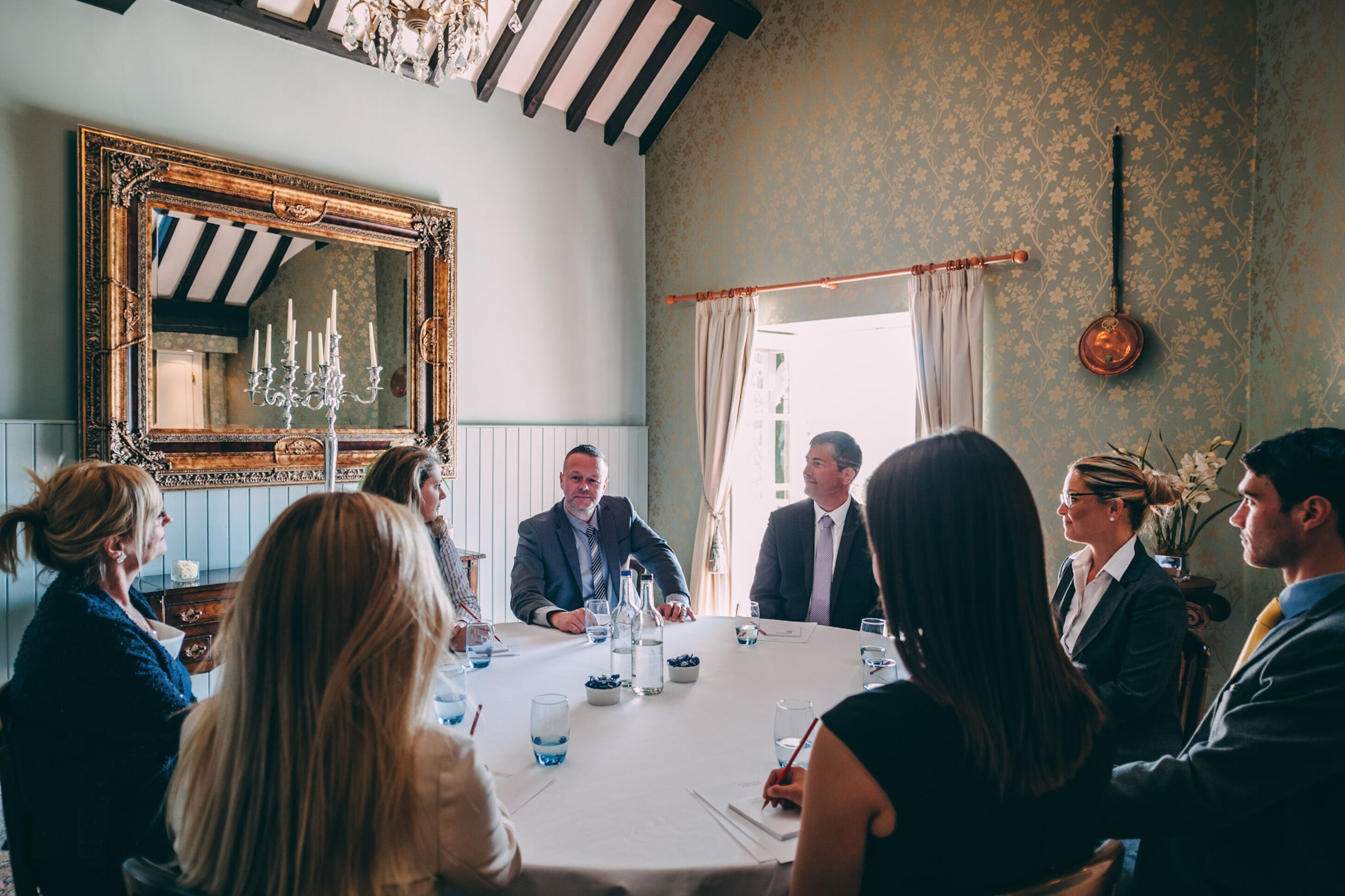 A formal meeting room with a large mirror, elegant table settings, and a chandelier.