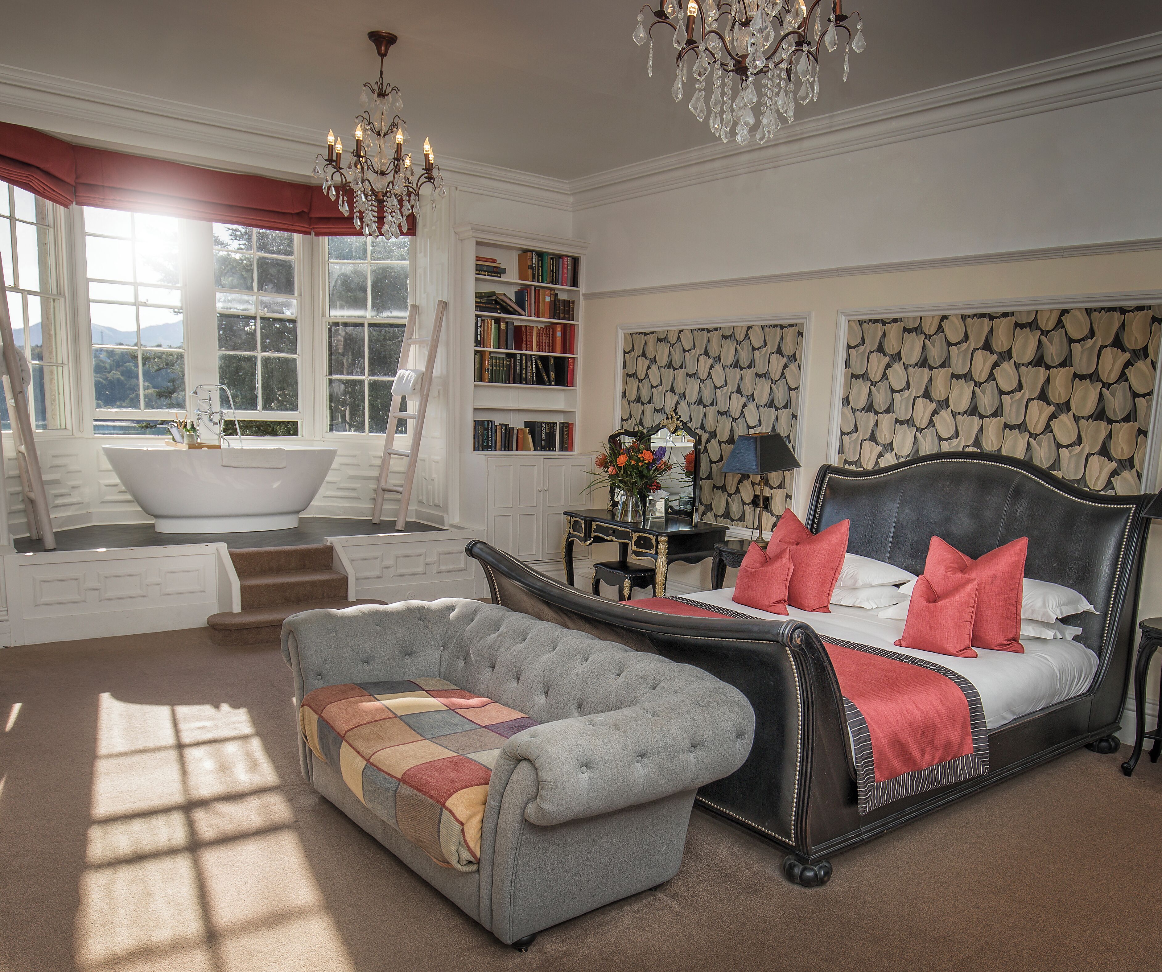 A bedroom with a large bed, a bathtub, a bookshelf, and a chandelier.