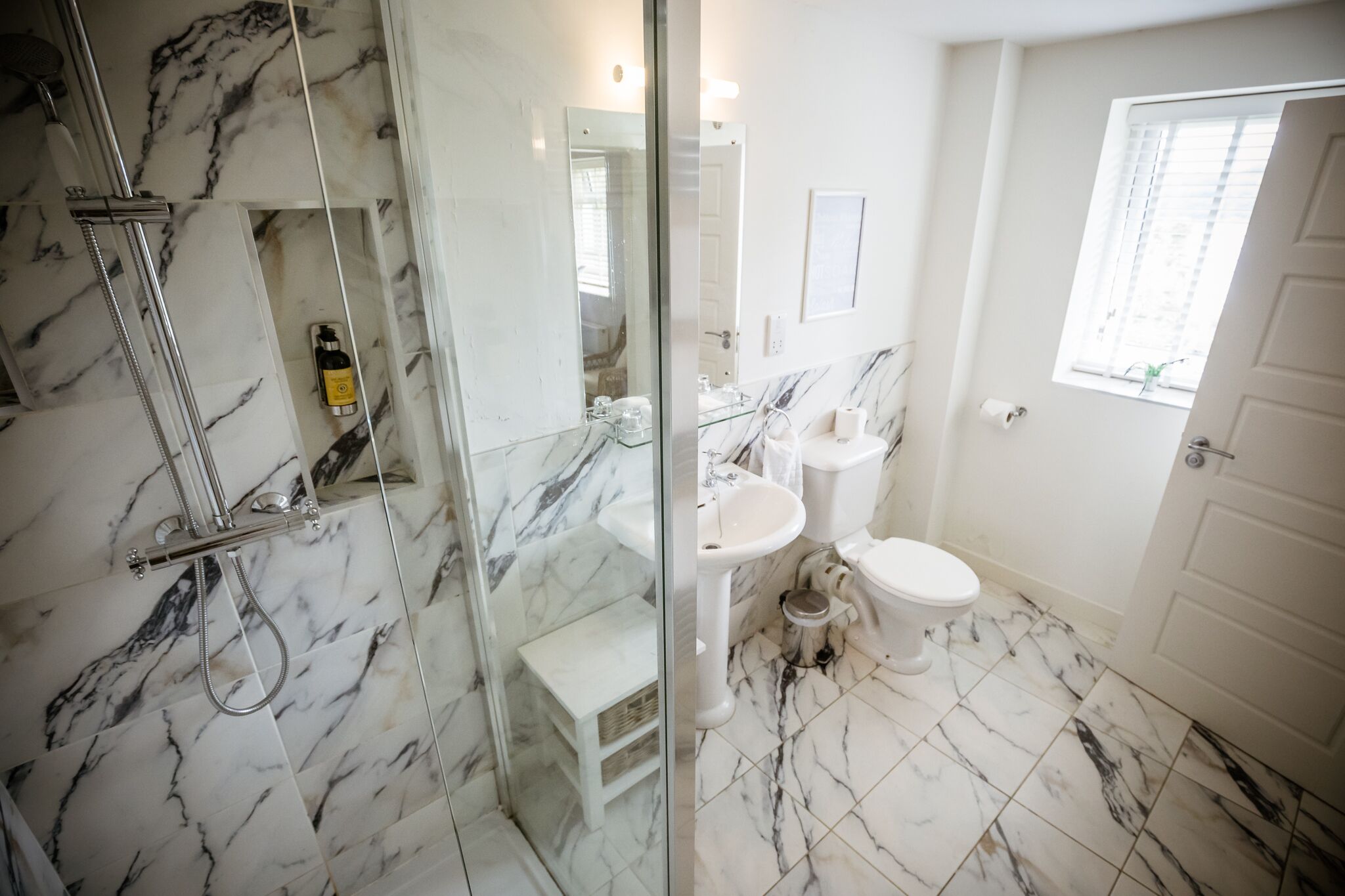 A bathroom with a glass shower enclosure, a white sink, a toilet, and a marble-tiled floor.