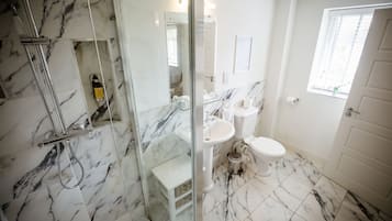 A bathroom with a glass shower enclosure, a white sink, a toilet, and a marble-tiled floor.
