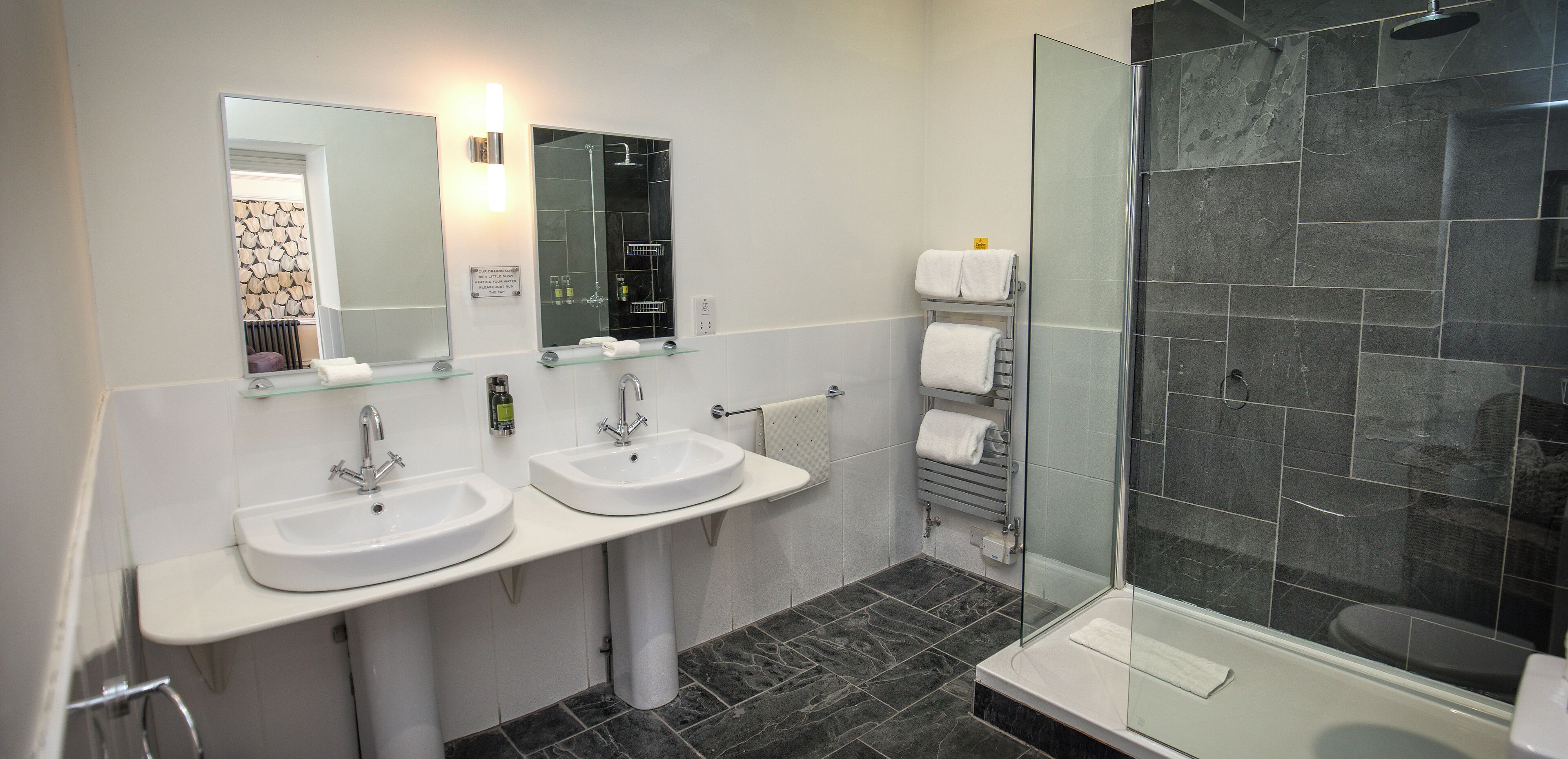 A modern bathroom with two sinks, a glass shower enclosure, and a towel rack.