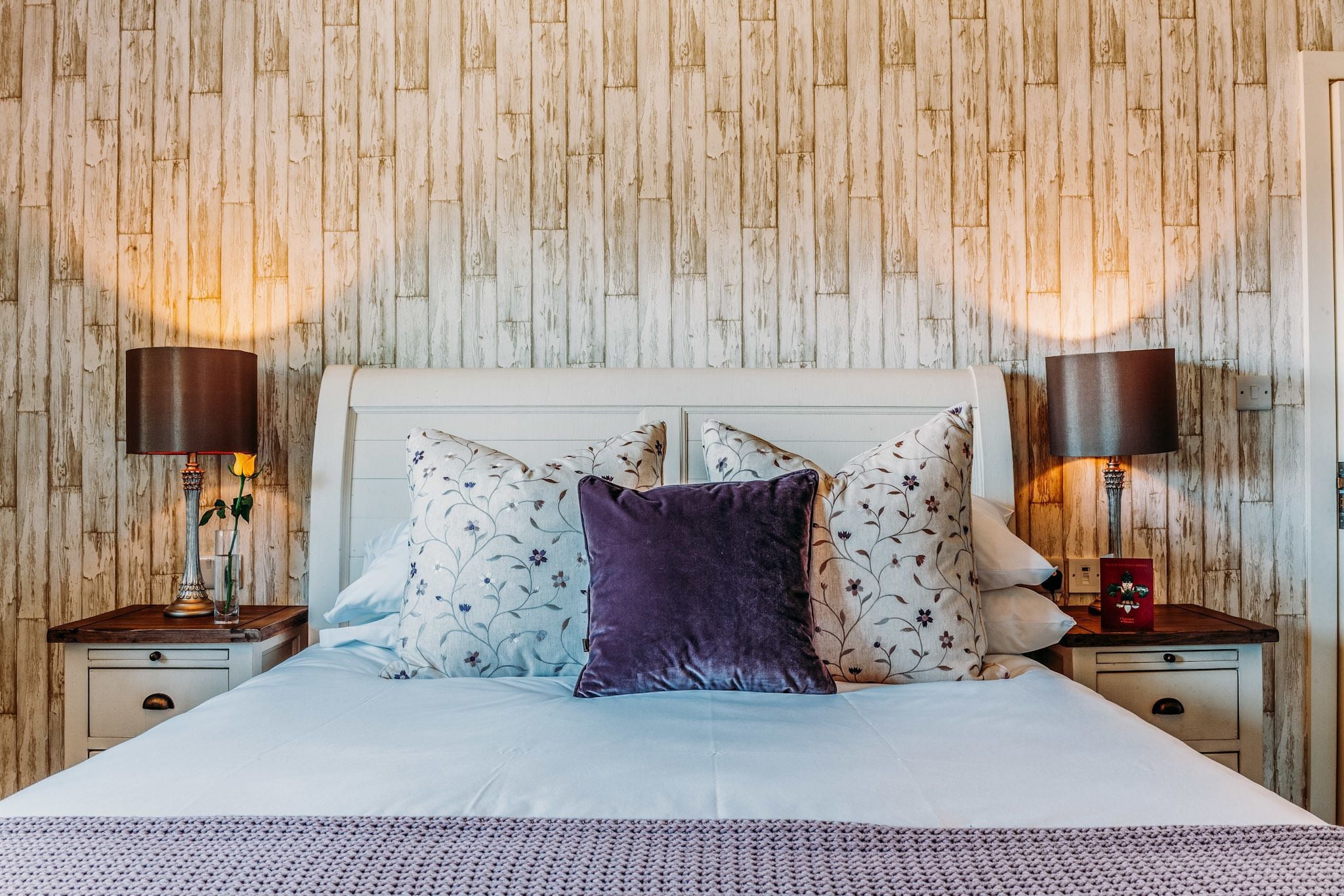 A neatly made bed with a white headboard, two nightstands with lamps, and a floral-patterned pillow.