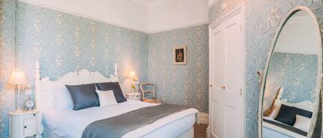 A bedroom with a large bed, two bedside tables with lamps, a wardrobe, and a mirror.
