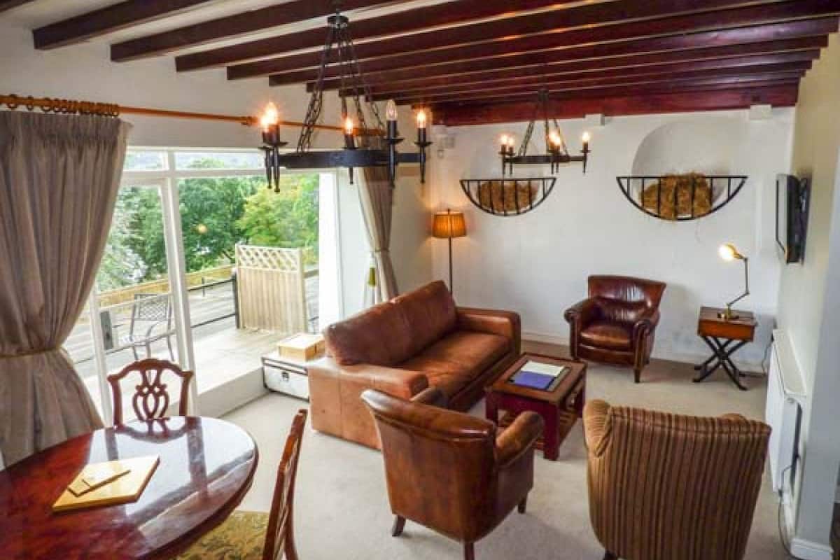 Un salón con techo de madera, mobiliario de cuero, una araña y vistas a zonas verdes.