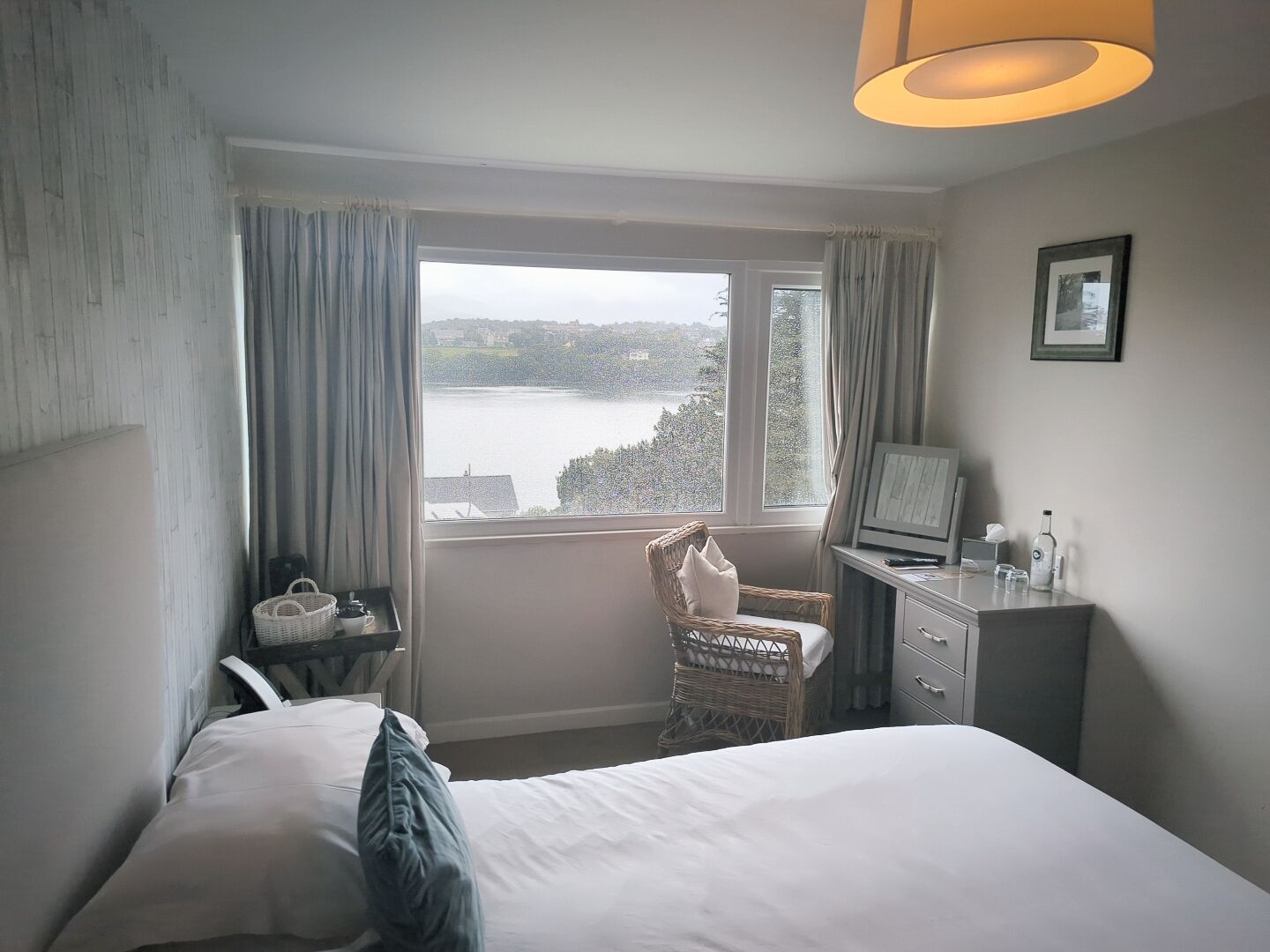 Un dormitorio con cama, escritorio, silla, televisor y ventana con vista al agua.