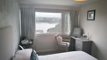 A bedroom with a bed, a desk, a chair, a television, and a window with a view of a body of water.