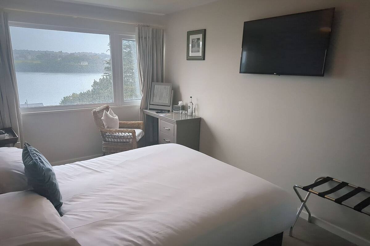 Habitación de hotel con cama, escritorio, silla, televisor y ventana con vista al lago.
