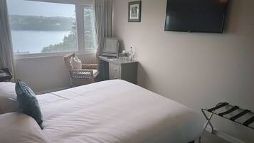 A hotel room with a bed, a desk, a chair, a TV, and a window with a view of a lake.