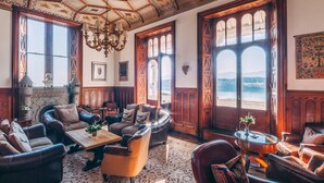 Amplia habitación con sofás de cuero, una mesa de centro de madera y grandes ventanas con vistas al mar.