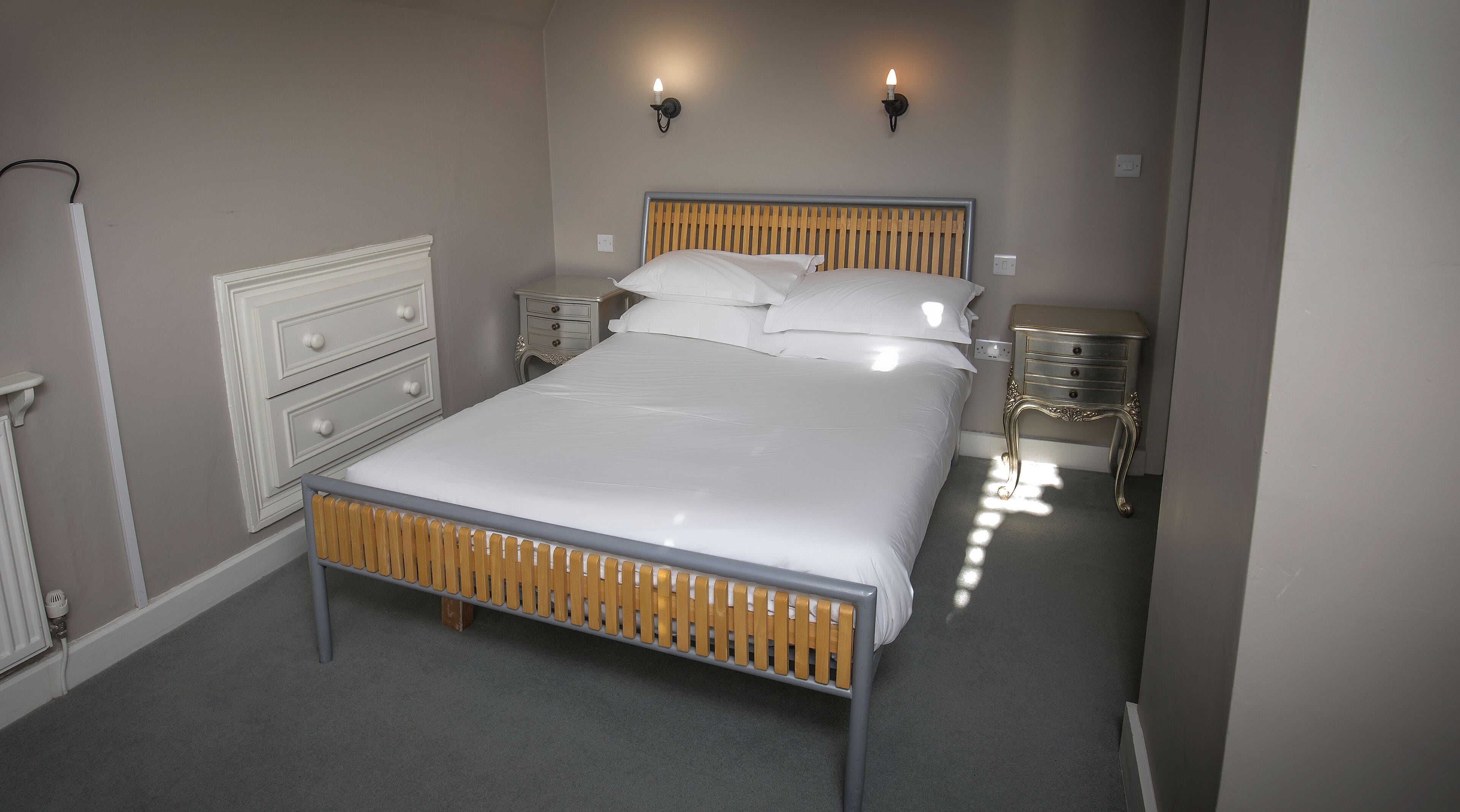 A neatly made bed with a wooden headboard, two bedside tables with lamps, and a white dresser with drawers.