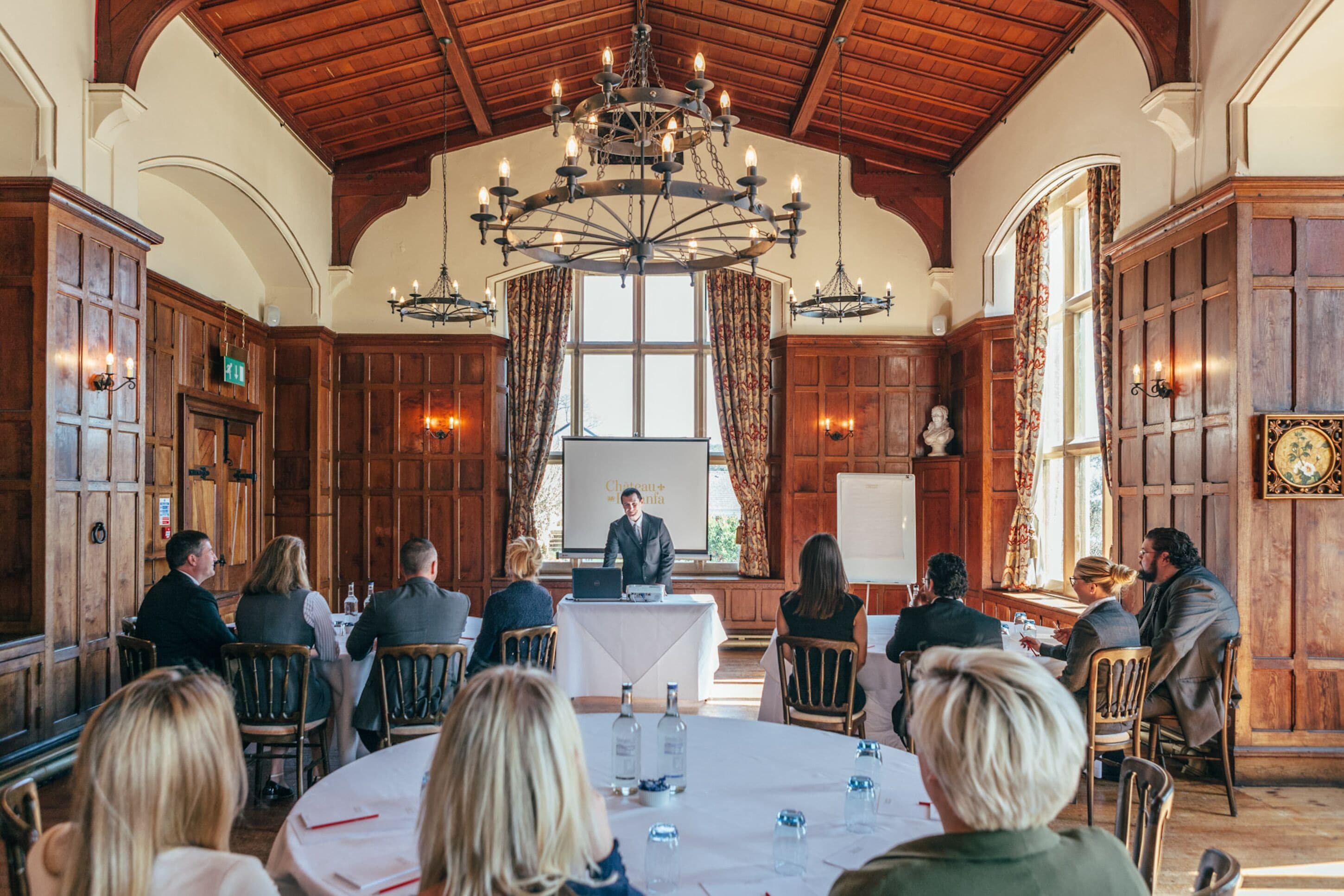 A conference room with wooden paneling, a large chandelier, and a presentation screen.