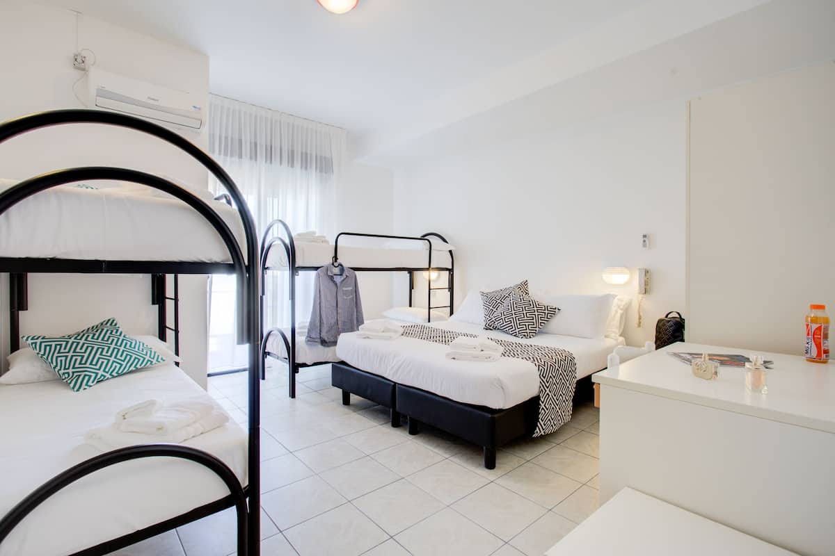 A hotel room with two bunk beds, a single bed, a desk, and a bedside table.