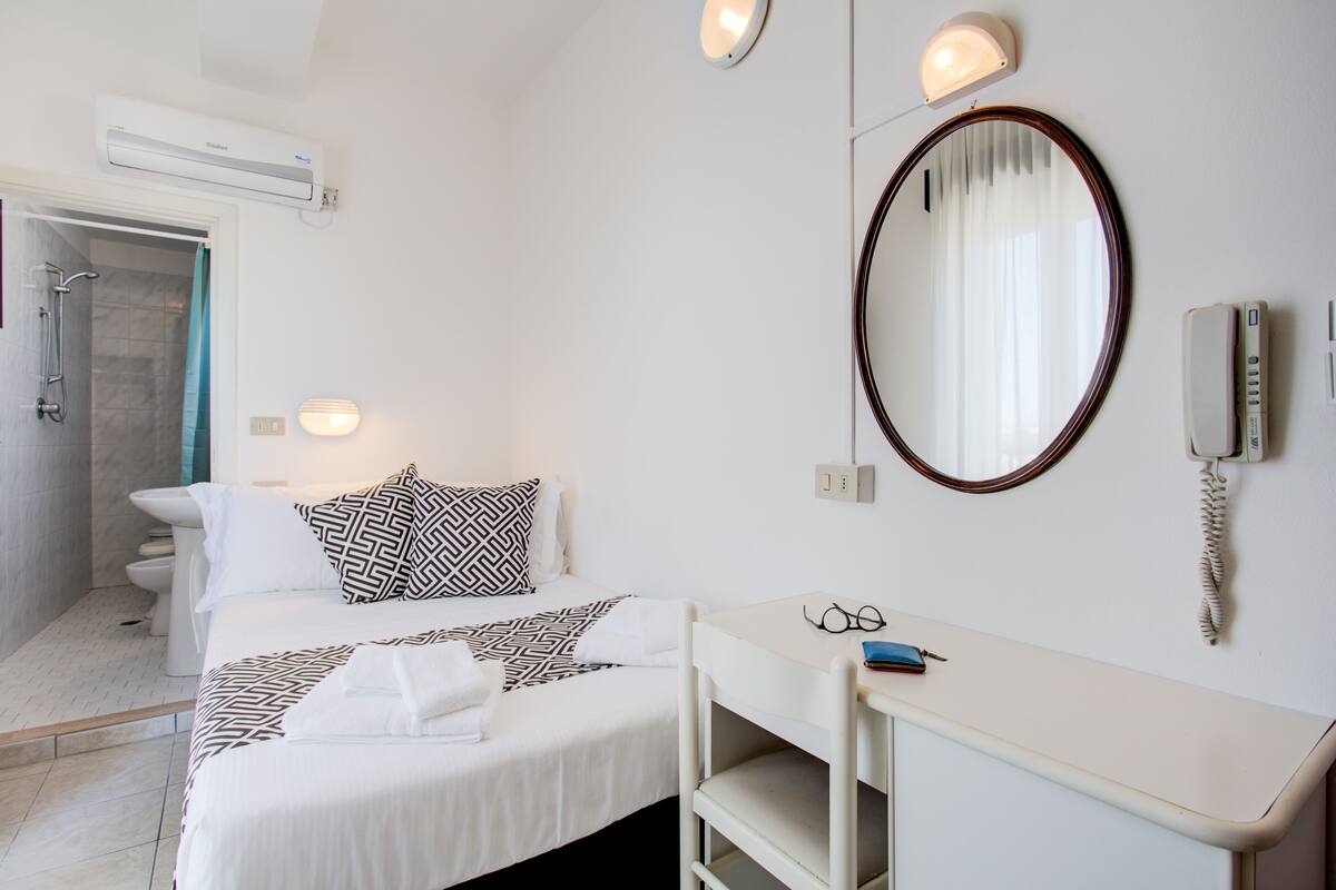 A hotel room with a bed, bedside table, mirror, and a bathroom with a shower.