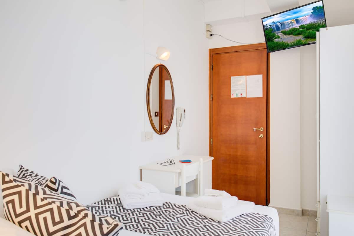 A hotel room with a bed, a desk, a mirror, a TV mounted on the wall, and a door.