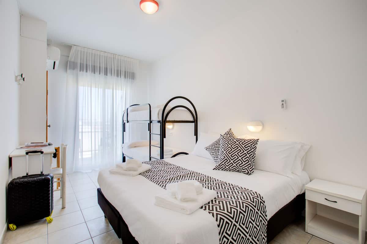 A hotel room with a bed, a desk, a chair, a suitcase, and a window with curtains.