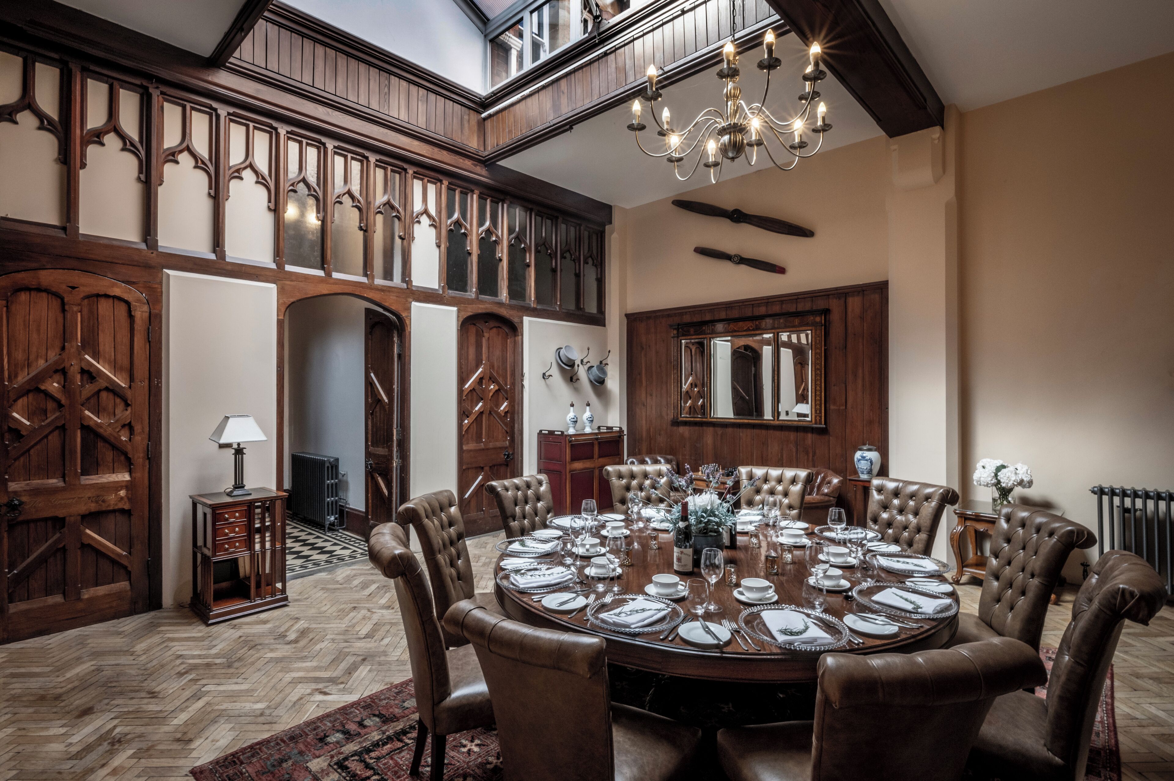 Comedor con una gran mesa redonda dispuesta para seis comensales, rodeada de sillas de cuero, un candelabro y paneles de madera.