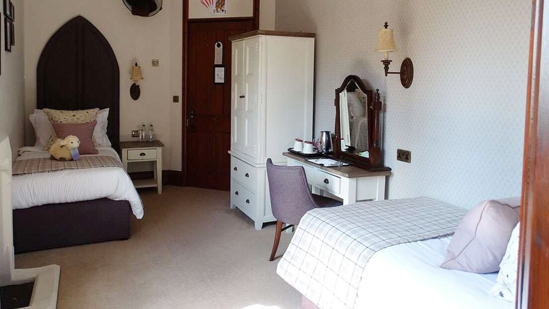 A bedroom with two beds, a desk, a wardrobe, and a mirror.