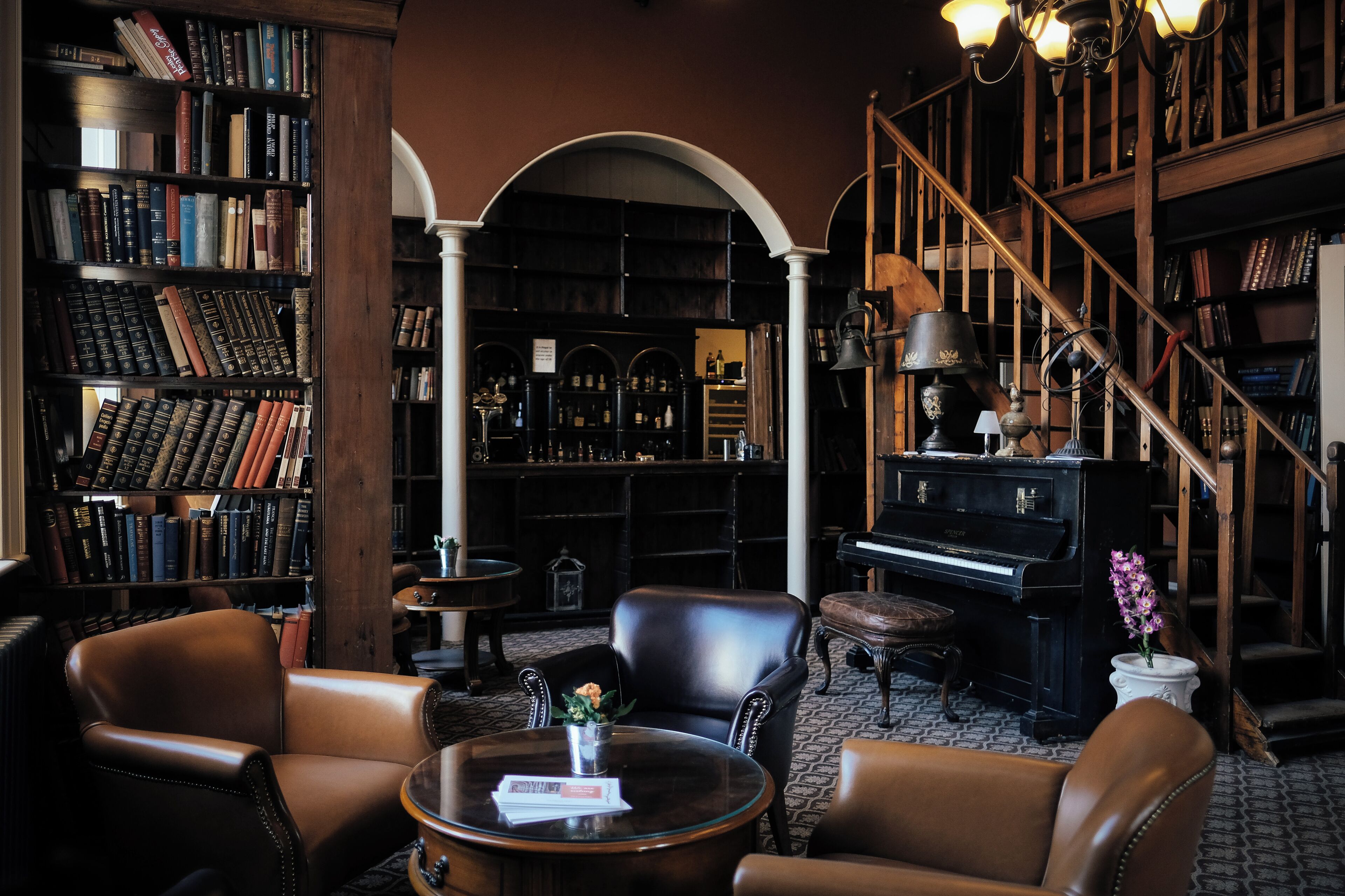 A library with bookshelves, a piano, leather chairs, and a coffee table.
