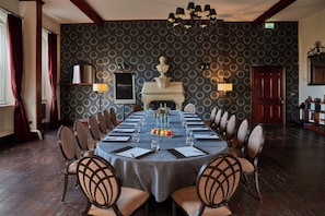 A formal dining room with a long table set for a meal, surrounded by chairs, a fireplace, and a patterned wall. - Stanbrook Abbey (Worcester)