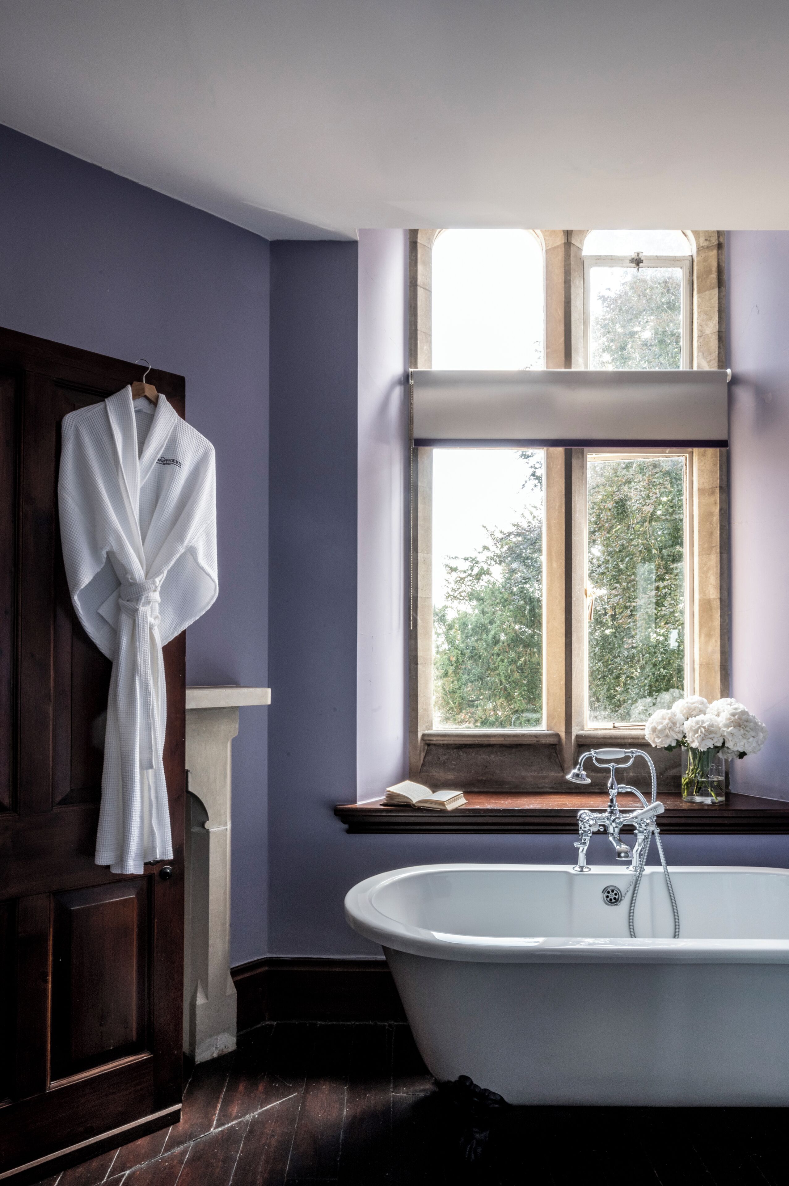 Un baño con bañera, una ventana con vistas a árboles y una bata colgada en la pared.